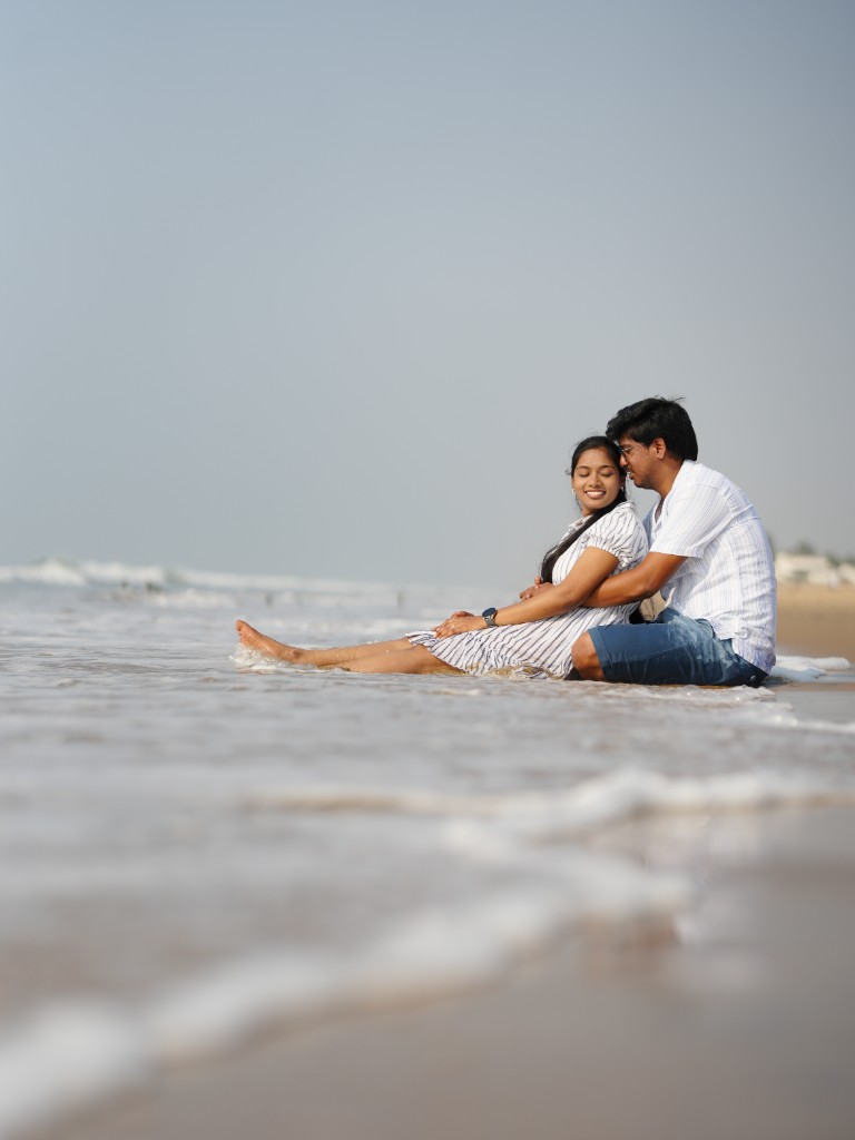 Couple sitting together at the shoreline with waves around them